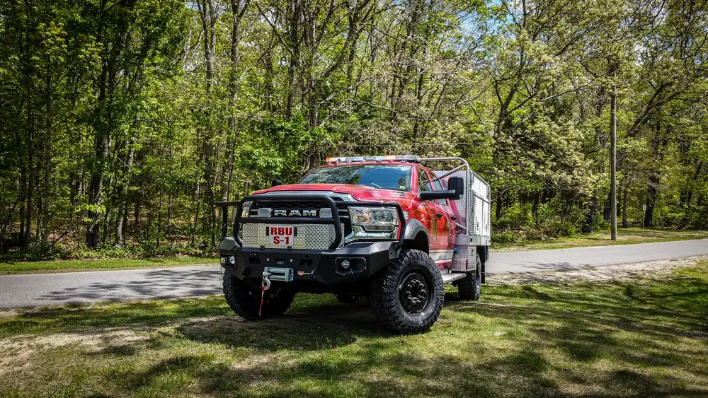 Exterior view of small fire truck showing cab, body compartments, and wheel/tire area.