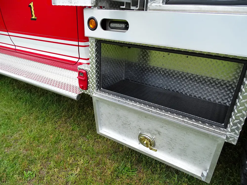 Exterior view of small fire truck showing cab, body compartments, and wheel/tire area.