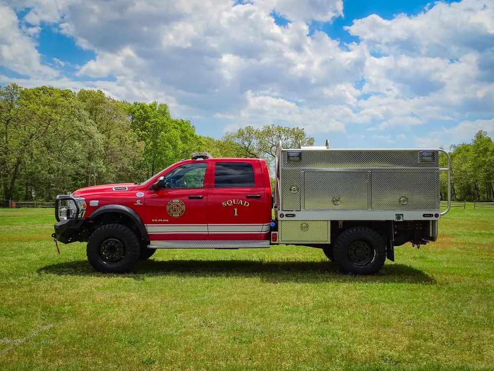 Exterior view of small fire truck showing cab, body compartments, and wheel/tire area.