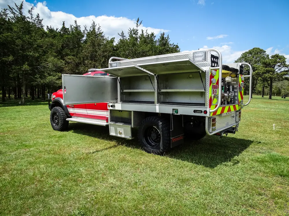 Exterior view of small fire truck showing cab, body compartments, and wheel/tire area.