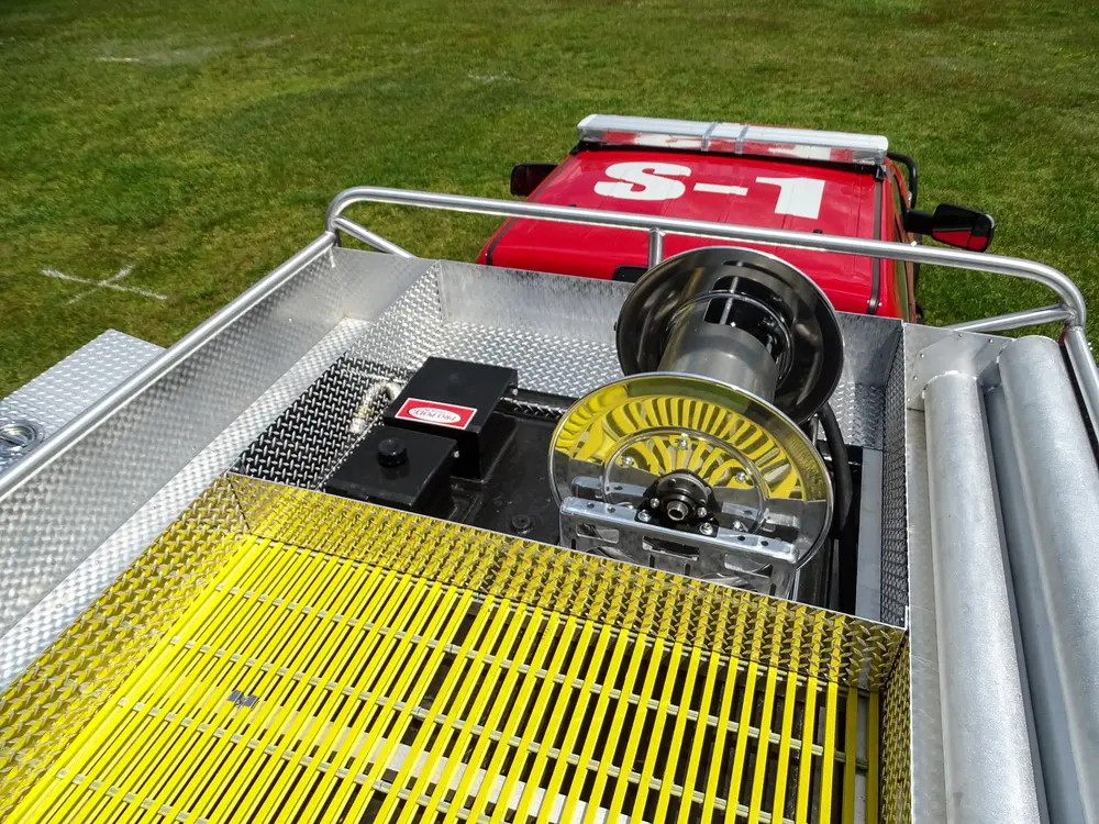 Exterior view of small fire truck showing cab, body compartments, and wheel/tire area.