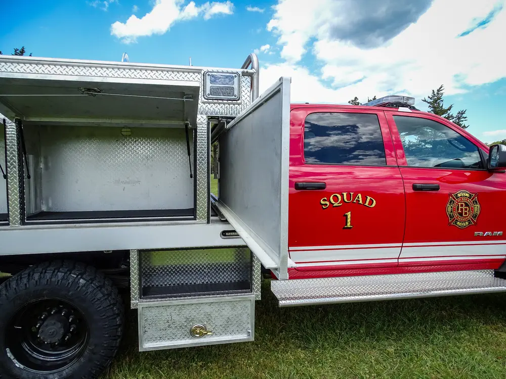 Exterior view of small fire truck showing cab, body compartments, and wheel/tire area.