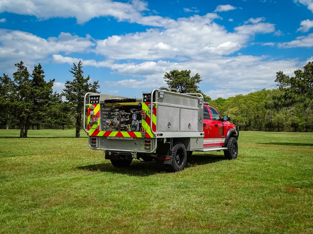 Exterior view of small fire truck showing cab, body compartments, and wheel/tire area.