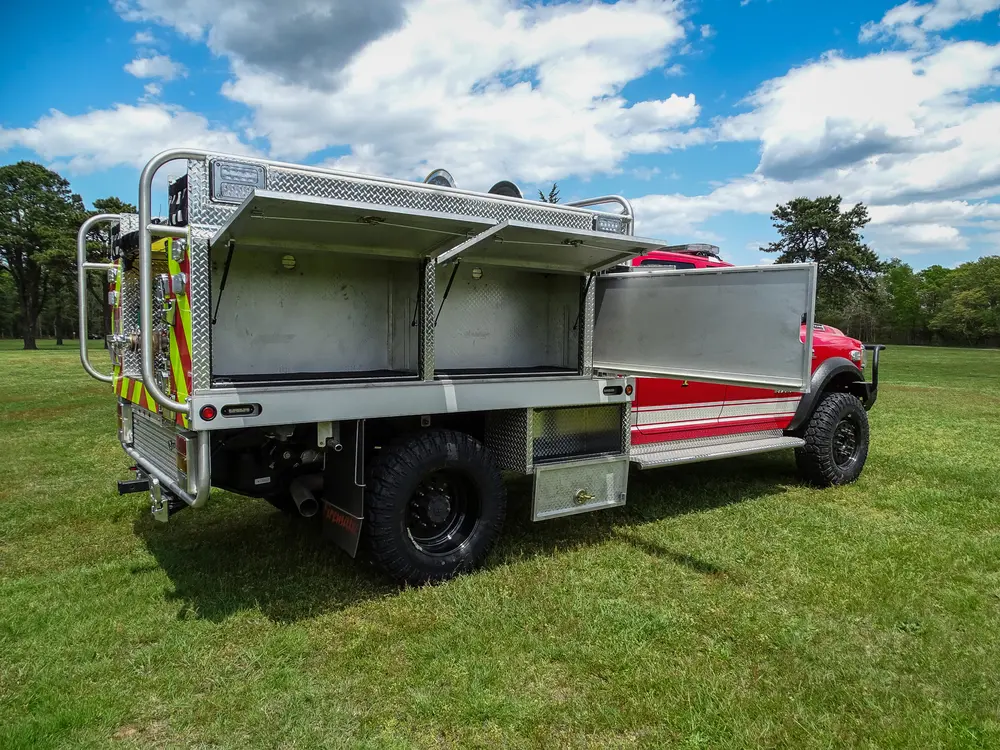 Exterior view of small fire truck showing cab, body compartments, and wheel/tire area.