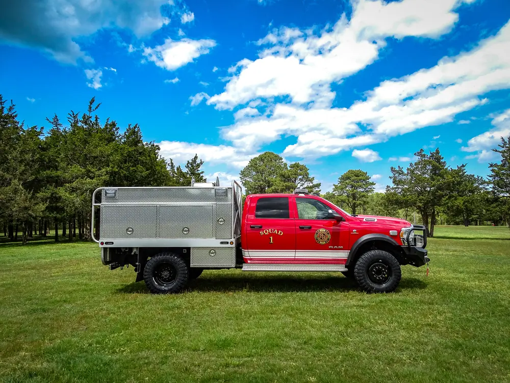 Exterior view of small fire truck showing cab, body compartments, and wheel/tire area.
