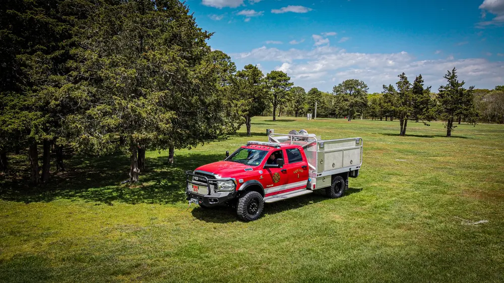 Exterior view of small fire truck showing cab, body compartments, and wheel/tire area.