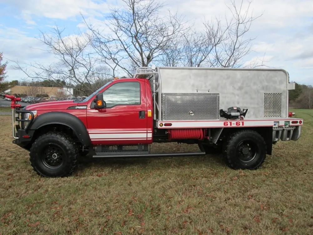 Exterior view of small fire truck showing cab, body compartments, and wheel/tire area.