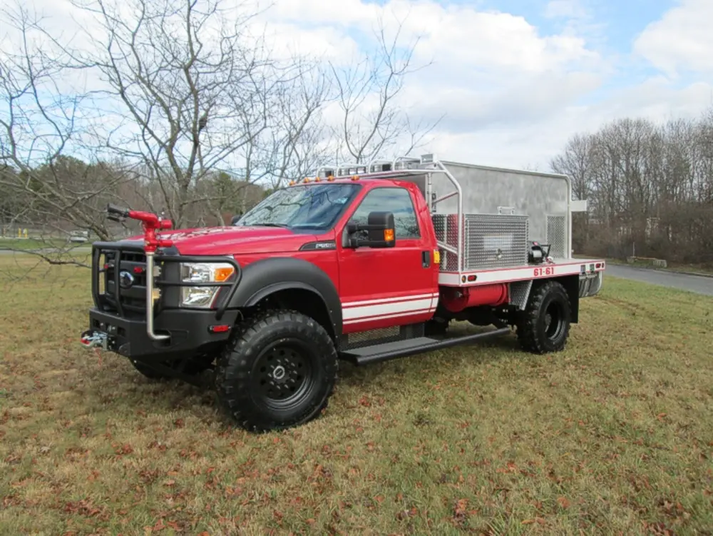Exterior view of small fire truck showing cab, body compartments, and wheel/tire area.