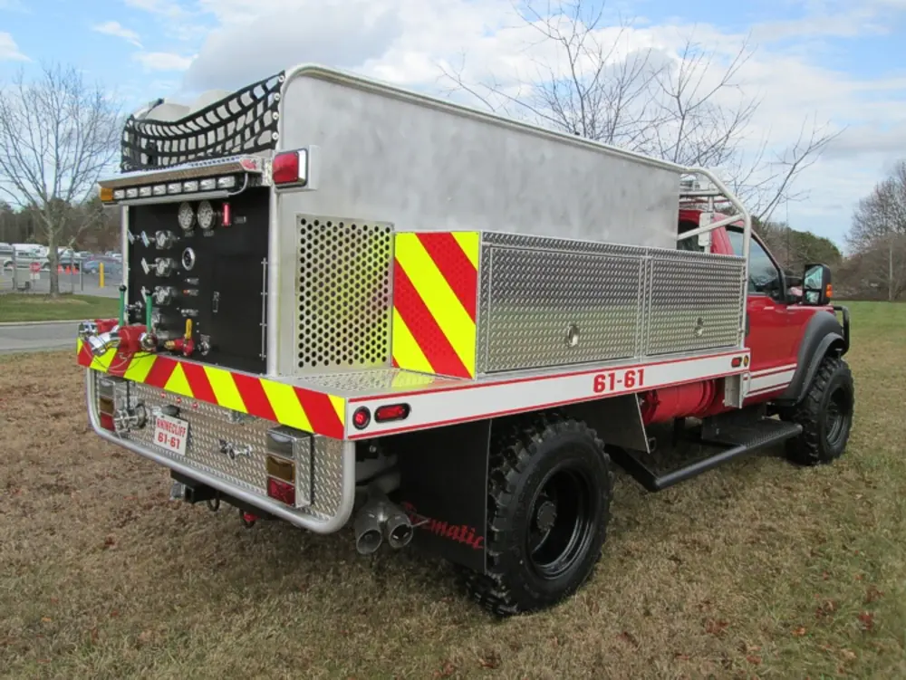 Exterior view of small fire truck showing cab, body compartments, and wheel/tire area.