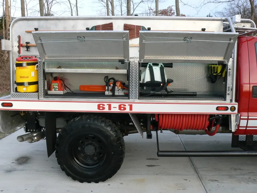 Exterior view of small fire truck showing cab, body compartments, and wheel/tire area.