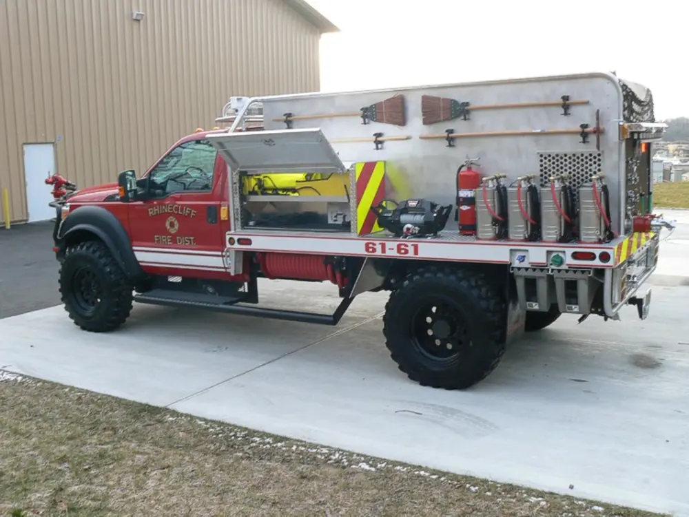 Exterior view of small fire truck showing cab, body compartments, and wheel/tire area.