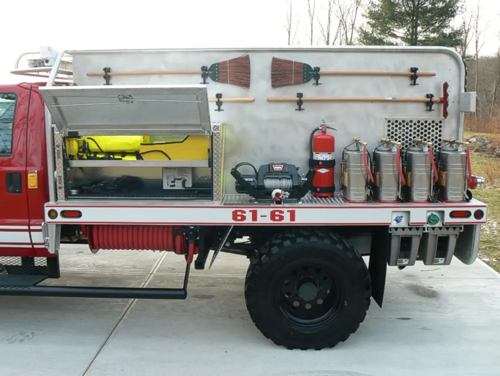 Exterior view of small fire truck showing cab, body compartments, and wheel/tire area.