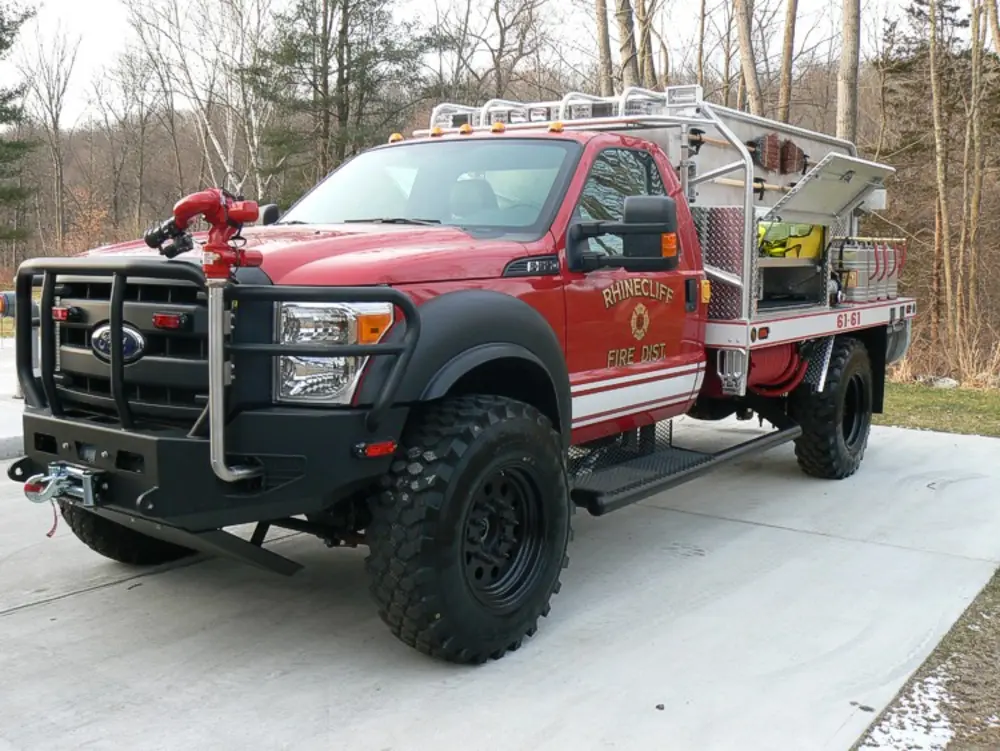 Exterior view of small fire truck showing cab, body compartments, and wheel/tire area.