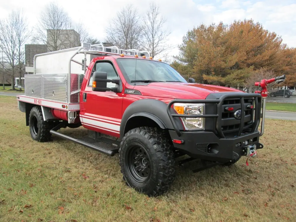Exterior view of small fire truck showing cab, body compartments, and wheel/tire area.