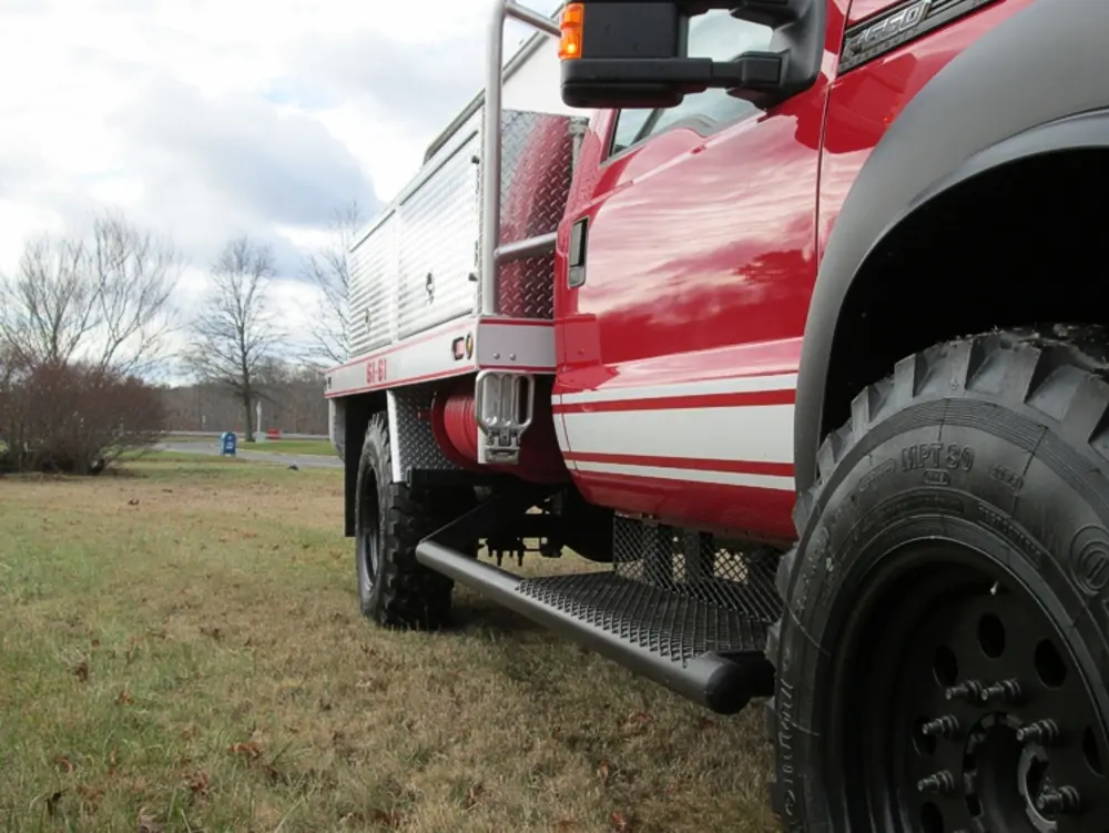 Exterior view of small fire truck showing cab, body compartments, and wheel/tire area.