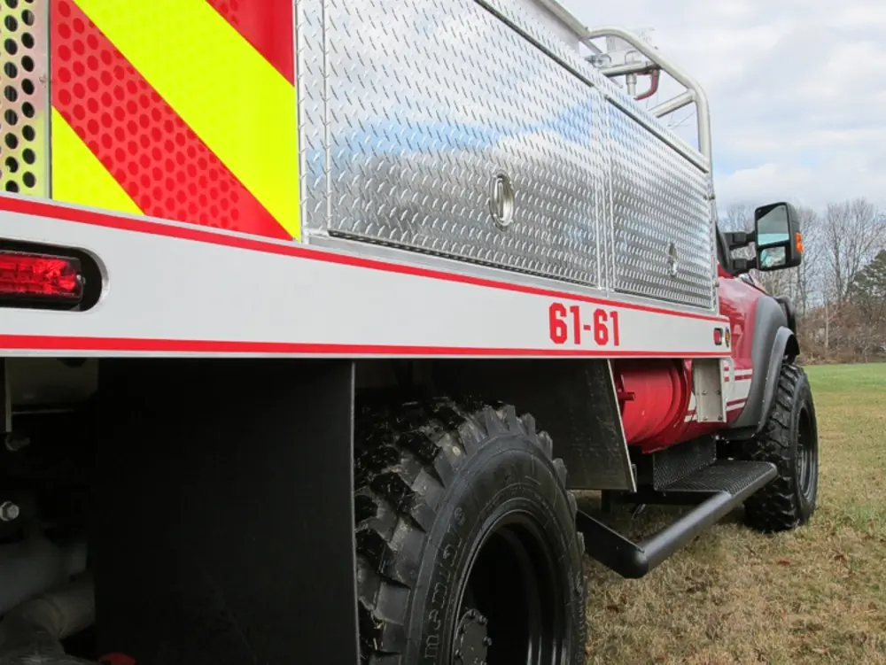 Exterior view of small fire truck showing cab, body compartments, and wheel/tire area.