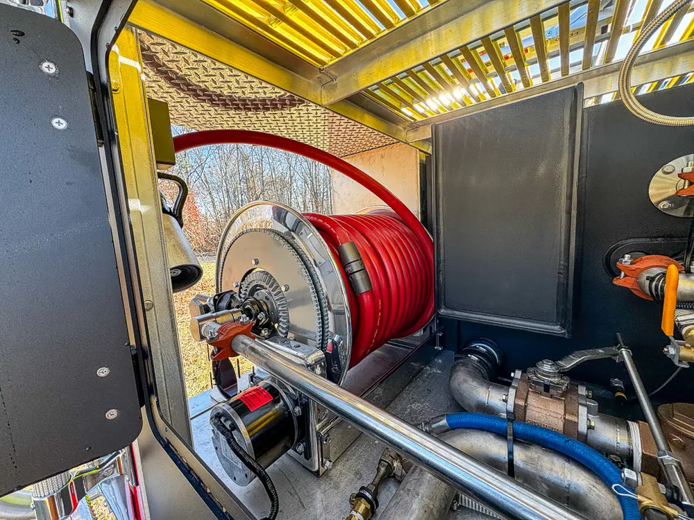 Pump compartment close-up with red hose reel, piping, and control hardware.
