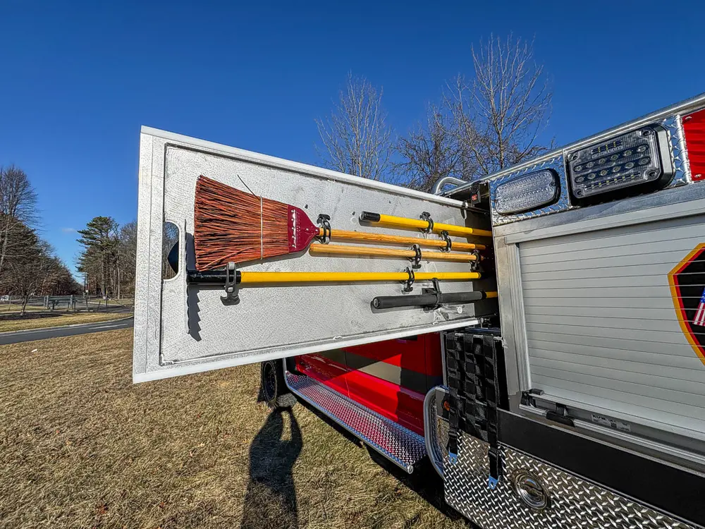 Open side door with mounted long-handled tools on interior brackets.