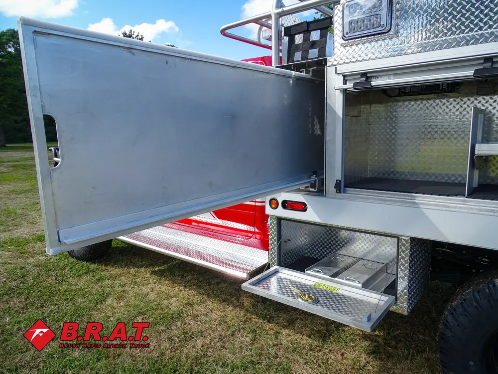 Exterior view of small fire truck showing cab, body compartments, and wheel/tire area.