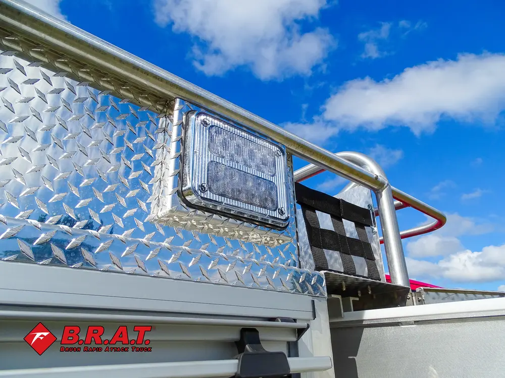 Exterior view of small fire truck showing cab, body compartments, and wheel/tire area.