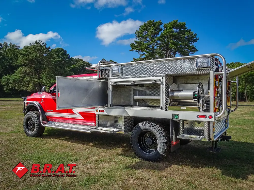 Exterior view of small fire truck showing cab, body compartments, and wheel/tire area.