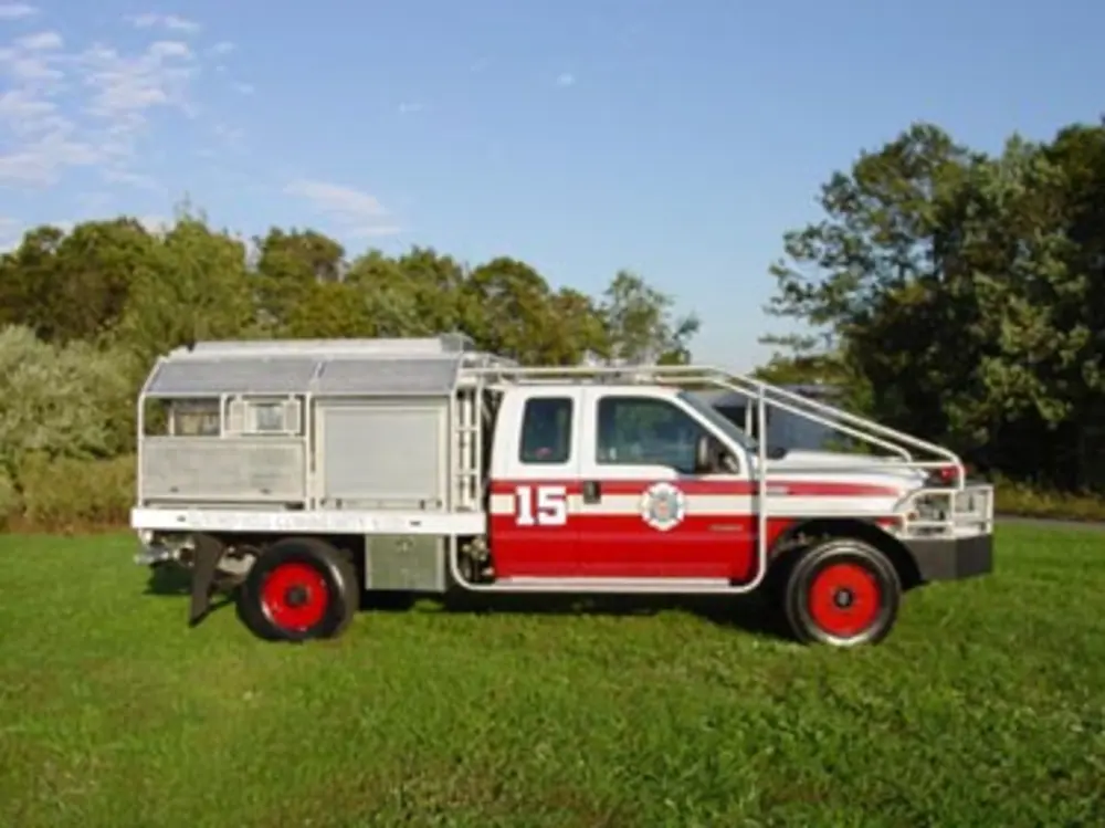 Exterior view of small fire truck showing cab, body compartments, and wheel/tire area.