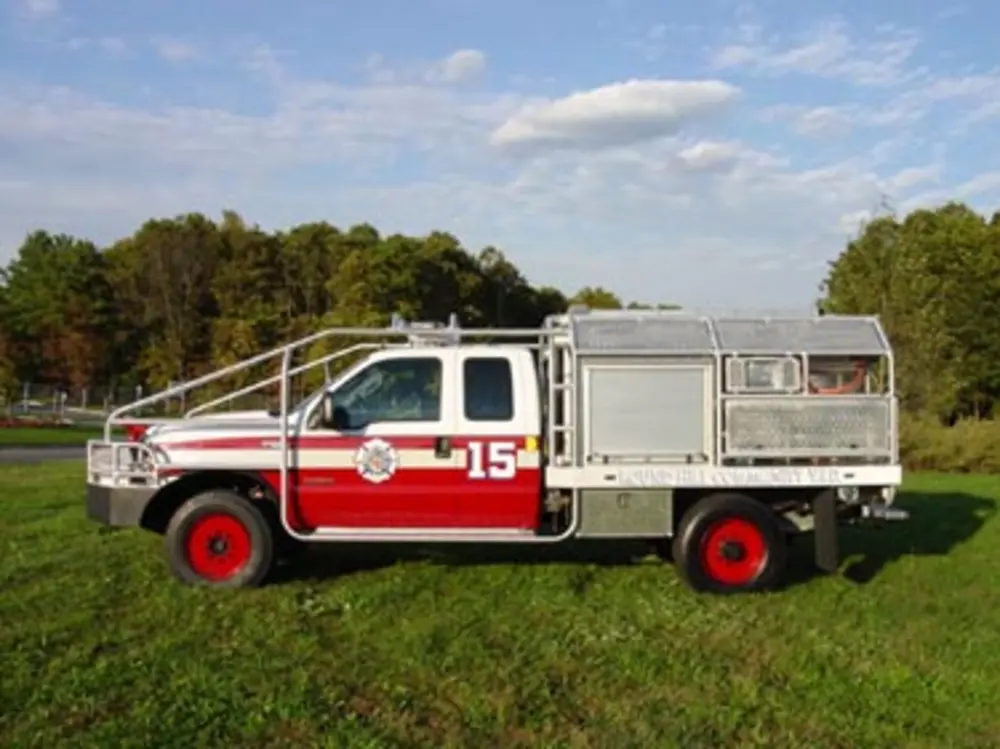 Exterior view of small fire truck showing cab, body compartments, and wheel/tire area.