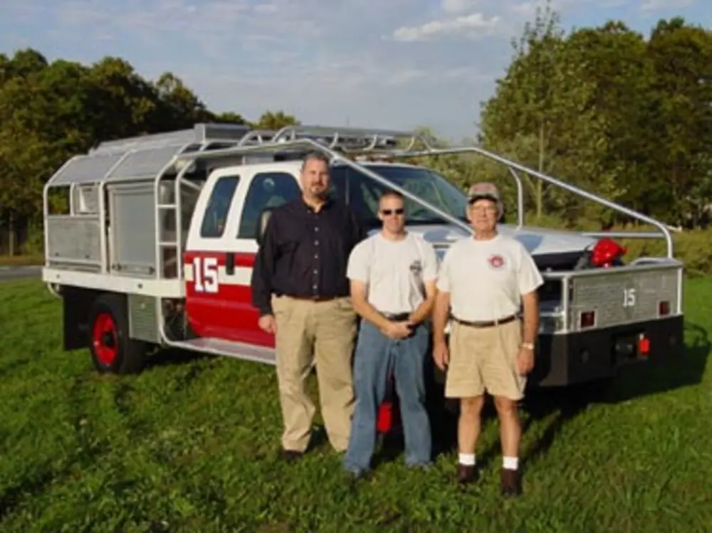 Exterior view of small fire truck showing cab, body compartments, and wheel/tire area.