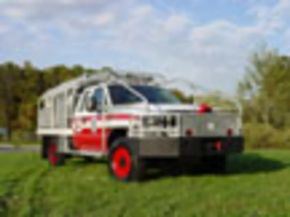 Exterior view of small fire truck showing cab, body compartments, and wheel/tire area.