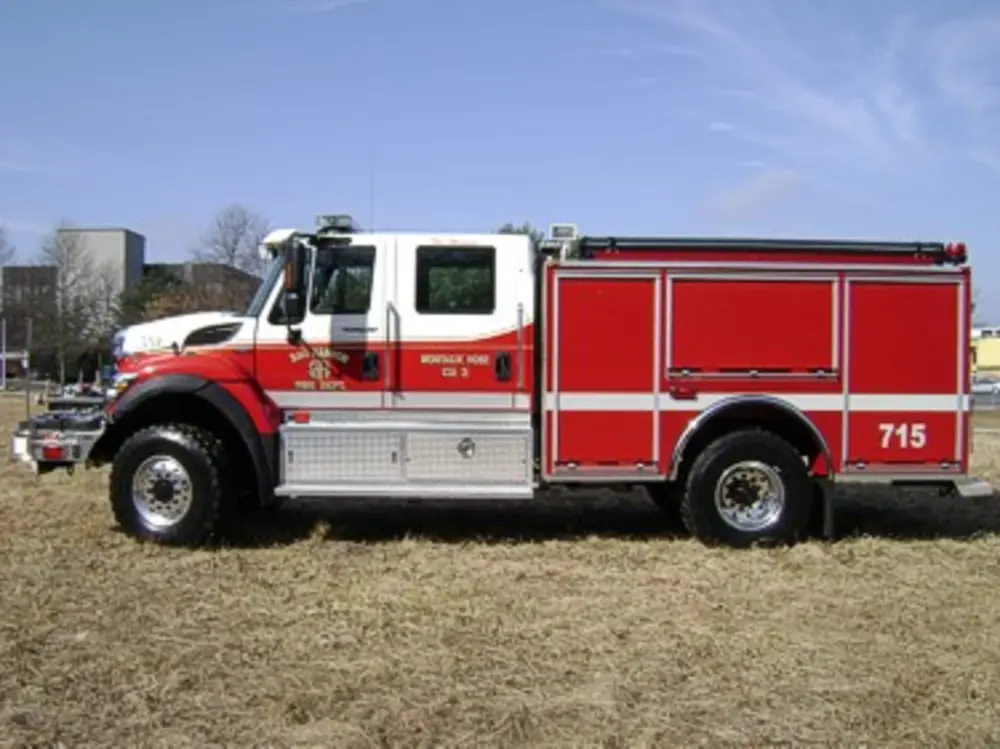 Exterior view of small fire truck showing cab, body compartments, and wheel/tire area.