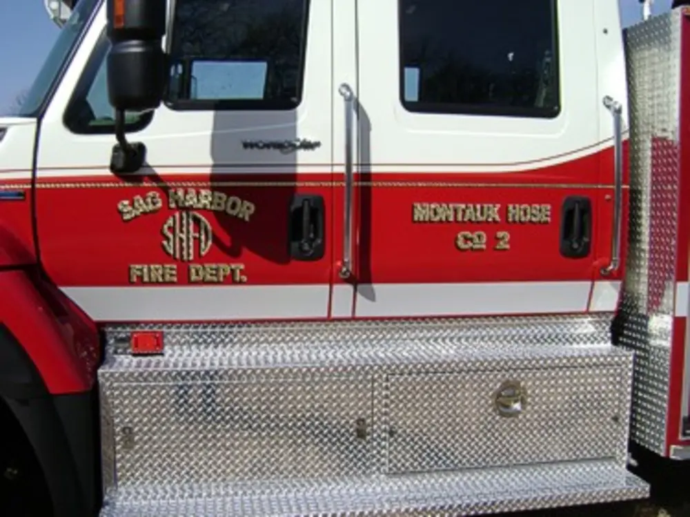 Exterior view of small fire truck showing cab, body compartments, and wheel/tire area.