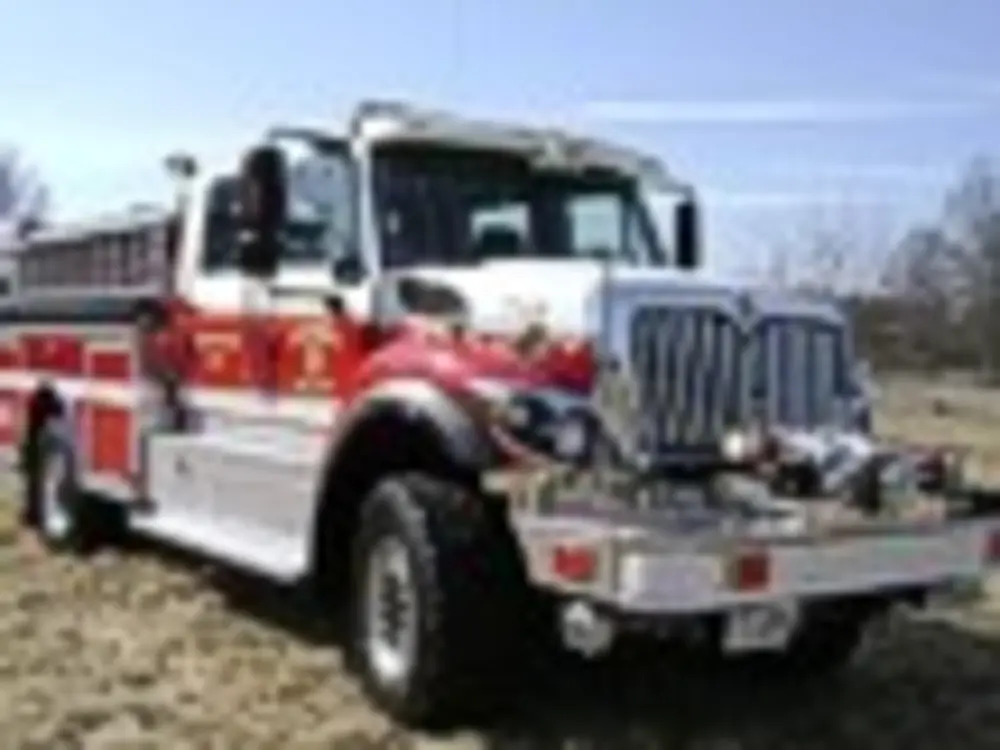 Exterior view of small fire truck showing cab, body compartments, and wheel/tire area.