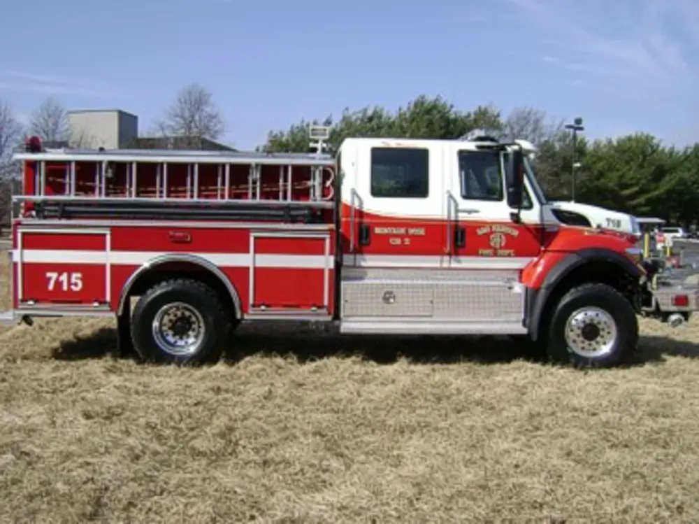 Exterior view of small fire truck showing cab, body compartments, and wheel/tire area.