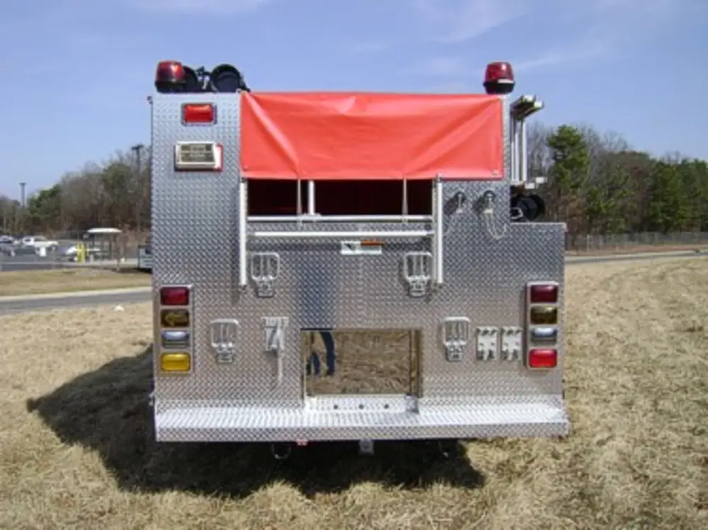 Exterior view of small fire truck showing cab, body compartments, and wheel/tire area.
