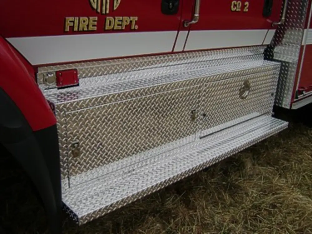 Exterior view of small fire truck showing cab, body compartments, and wheel/tire area.