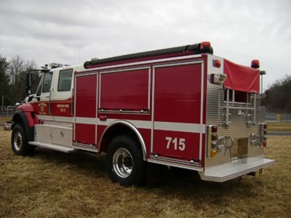 Exterior view of small fire truck showing cab, body compartments, and wheel/tire area.