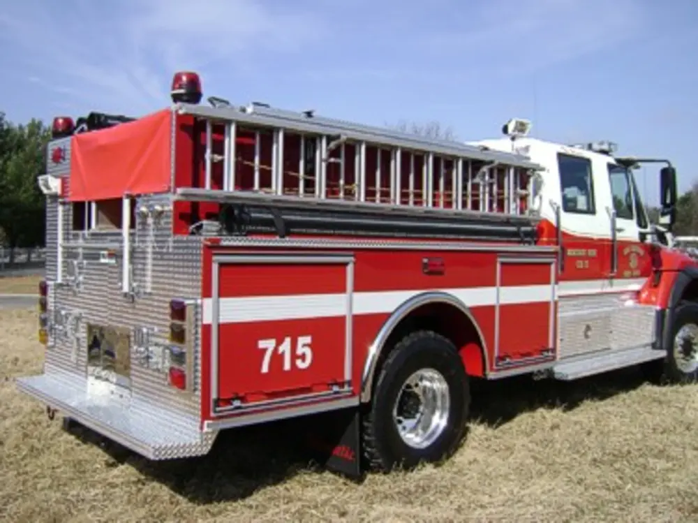 Exterior view of small fire truck showing cab, body compartments, and wheel/tire area.