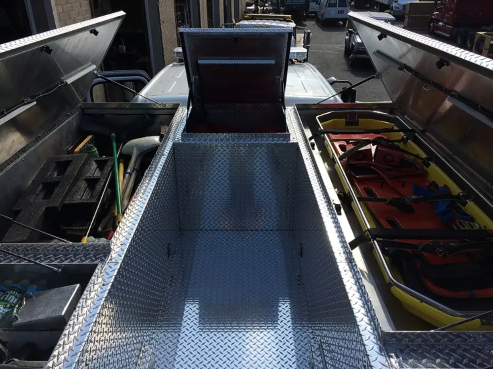 Exterior view of small fire truck showing cab, body compartments, and wheel/tire area.