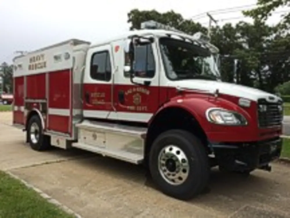 Exterior view of small fire truck showing cab, body compartments, and wheel/tire area.