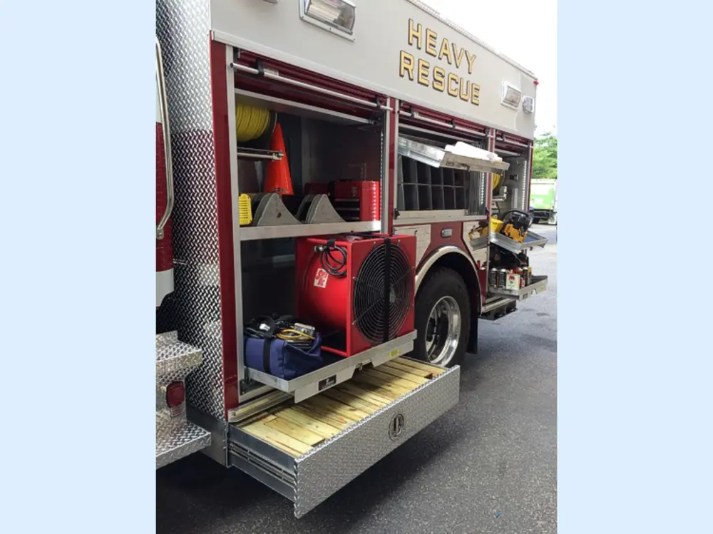 Exterior view of small fire truck showing cab, body compartments, and wheel/tire area.
