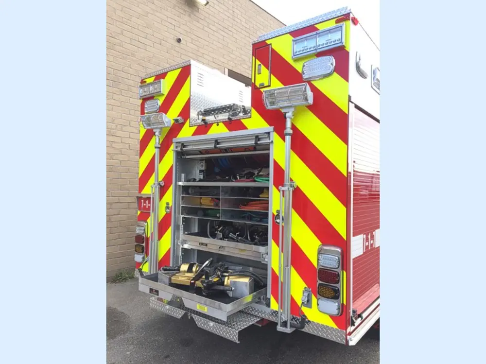 Exterior view of small fire truck showing cab, body compartments, and wheel/tire area.