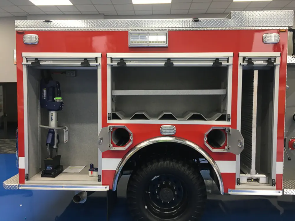 Exterior view of small fire truck showing cab, body compartments, and wheel/tire area.