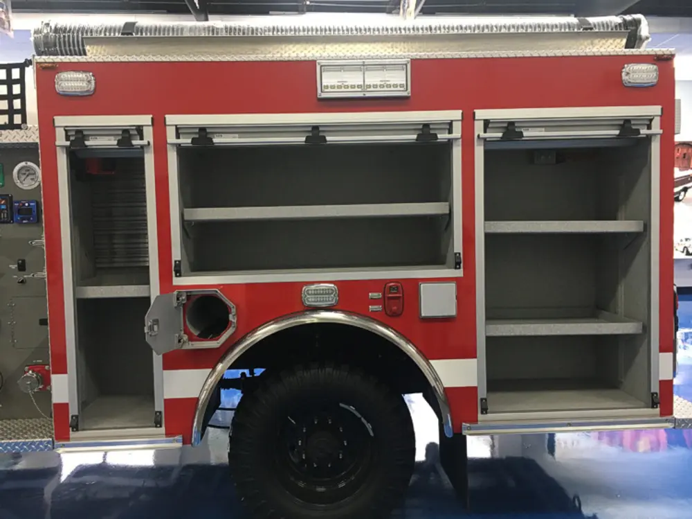 Exterior view of small fire truck showing cab, body compartments, and wheel/tire area.