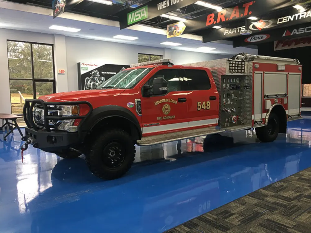 Exterior view of small fire truck showing cab, body compartments, and wheel/tire area.