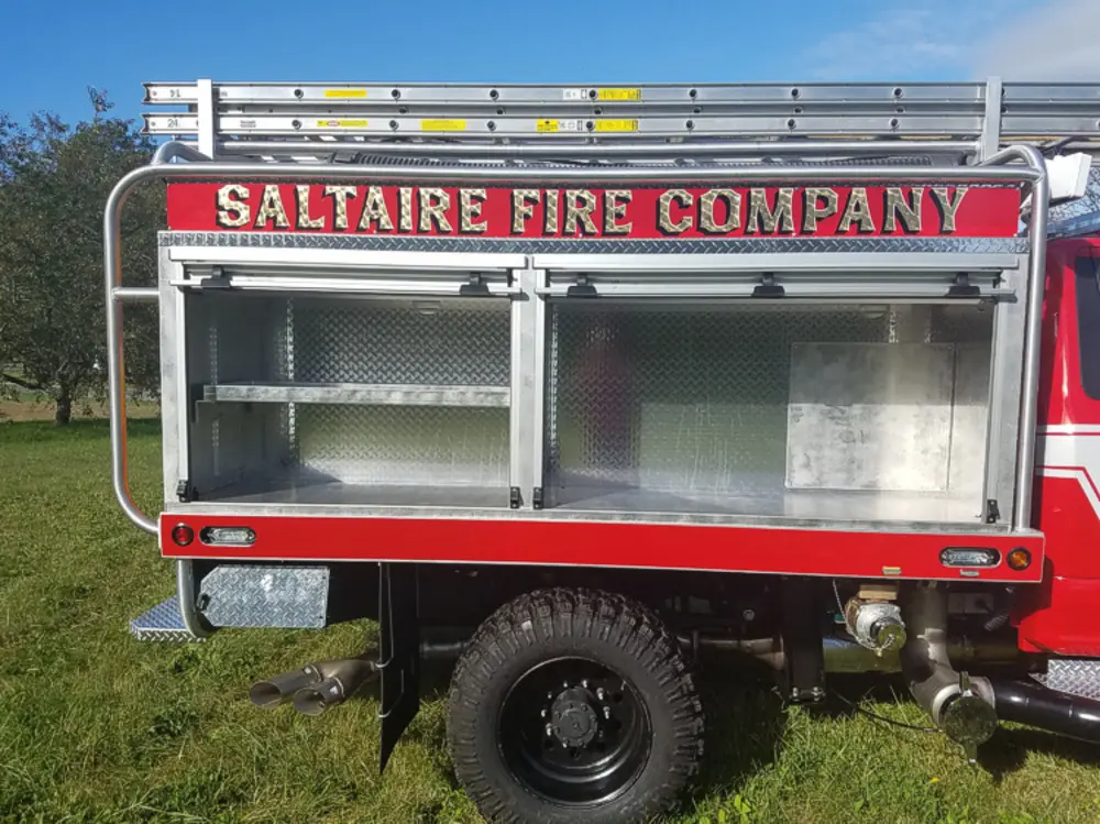 Exterior view of small fire truck showing cab, body compartments, and wheel/tire area.