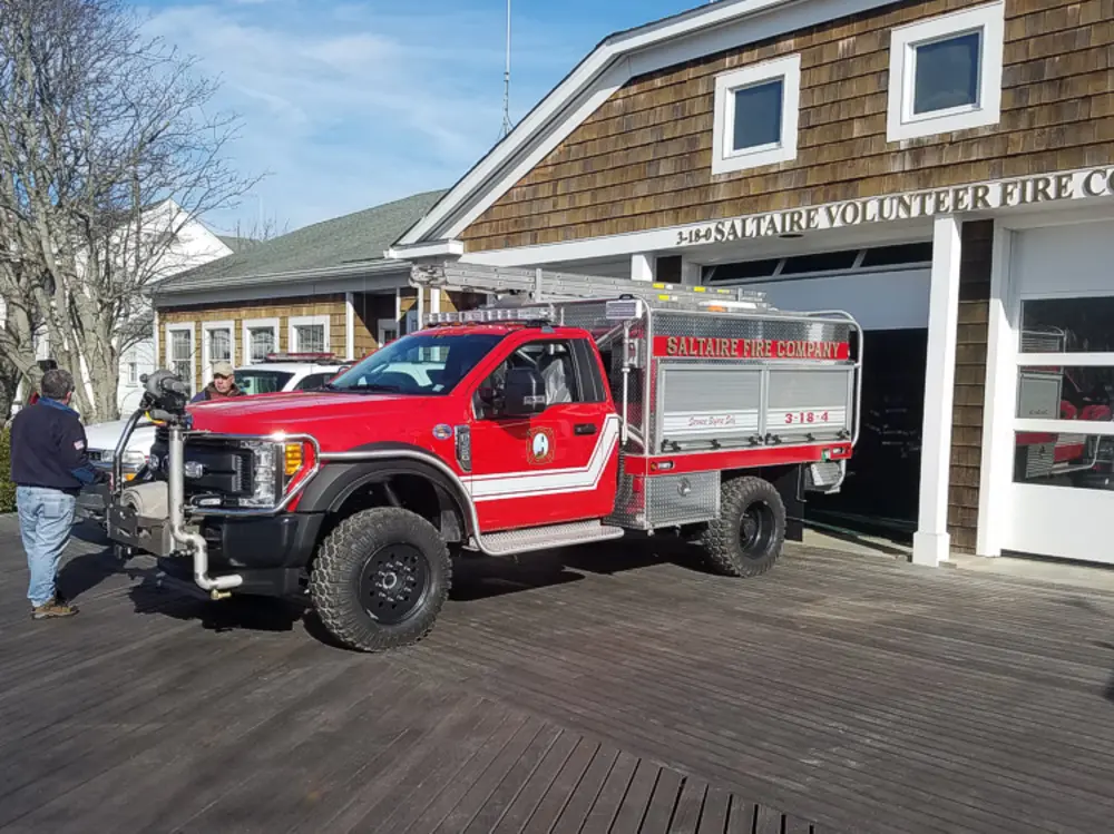 Exterior view of small fire truck showing cab, body compartments, and wheel/tire area.