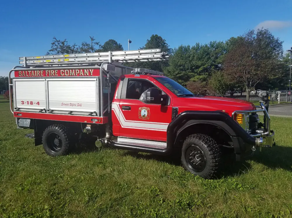 Exterior view of small fire truck showing cab, body compartments, and wheel/tire area.