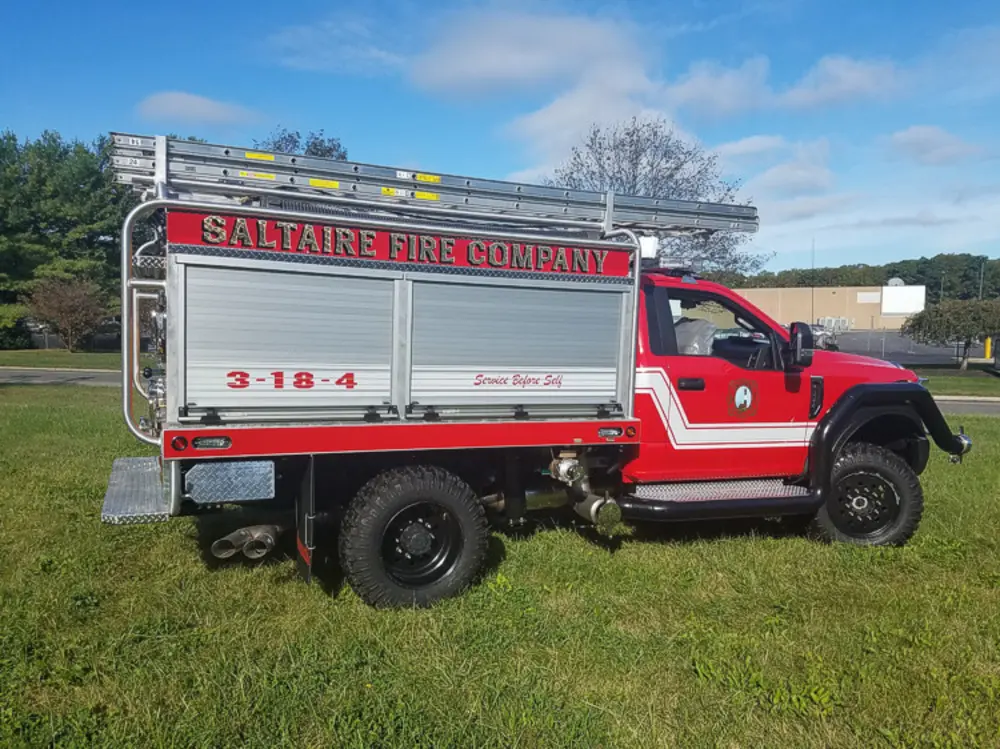 Exterior view of small fire truck showing cab, body compartments, and wheel/tire area.