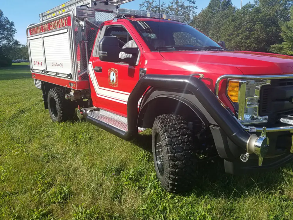 Exterior view of small fire truck showing cab, body compartments, and wheel/tire area.