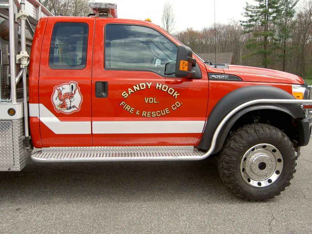 Exterior view of small fire truck showing cab, body compartments, and wheel/tire area.